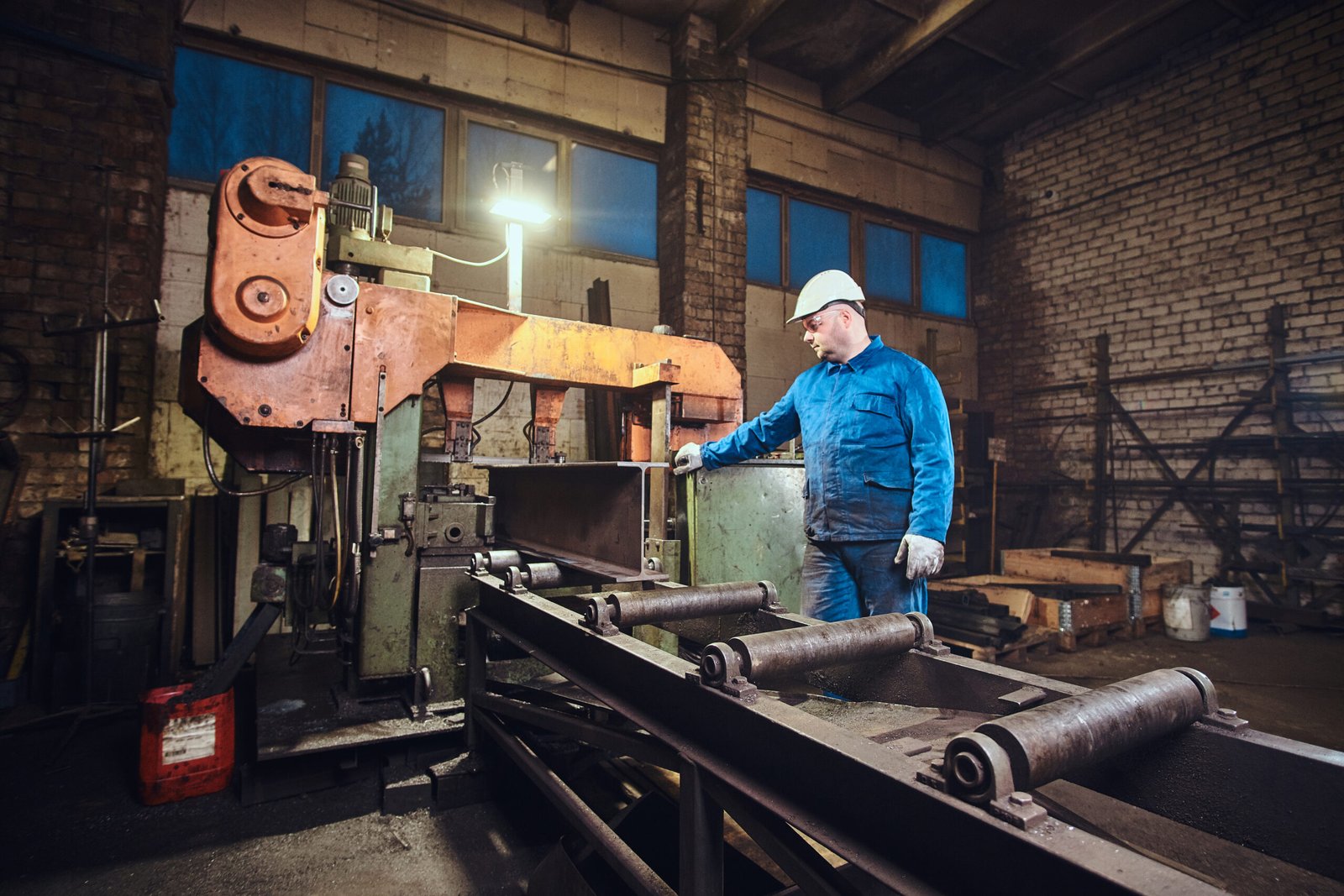 Worker is controlling a process of rail cutting at busy metal factory.